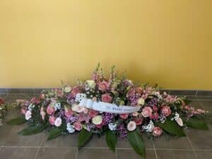 Composition florale de deuil rose, blanche, mauve avec feuilles. Ruban "A NOTRE MAMAN REGRETTEE".