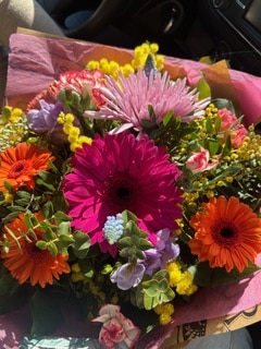 Bouquet éclatant de gerberas roses et oranges, chrysanthèmes et mimosas jaunes dans un emballage festif.