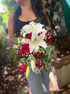 Bouquet de mariée composé de grands lys blancs, roses rouges éclatantes et gypsophile délicat tenu par une femme.