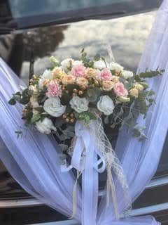 Bouquet de fleurs de mariage blanc et rose sur capot de voiture avec tulle vaporeux et rubans élégants.