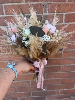 Bouquet bohème de fleurs séchées et herbe de la pampa avec ruban rose devant un mur de briques.