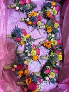 Boutonnières de mariage colorées avec roses roses, chardons bleus et craspedias jaunes, tiges entourées de ficelle.