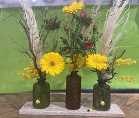 Bouquet printanier de gerberas jaunes et mimosas dans trois vases colorés, déco champêtre et lumineuse.