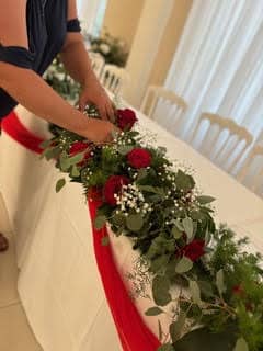 Mains agençant un centre de table floral avec roses rouges et feuillage pour une décoration de mariage élégante.