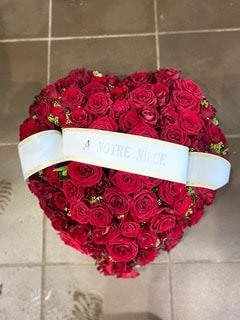 Cœur de roses rouges funéraire avec ruban blanc marqué À NOTRE NIÈCE. Composition florale de deuil élégante.