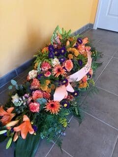 Composition florale funéraire de lys orange et roses roses avec ruban de deuil pour un dernier hommage lors d'obsèques.