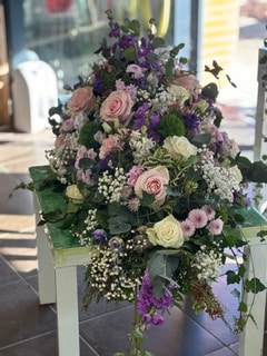 Grand bouquet funéraire de roses roses et blanches, fleurs violettes et gypsophile sur une table blanche.