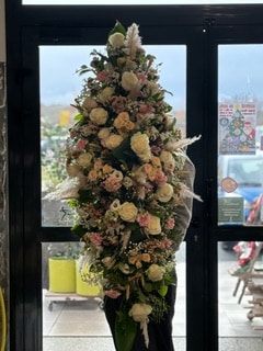 Grande composition florale verticale avec roses blanches, fleurs roses et pampas devant une porte de magasin.
