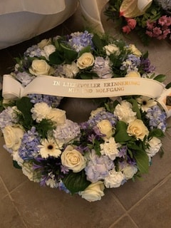 Couronne funéraire de roses blanches et hortensias bleus avec ruban 'IN LIEBEVOLLER ERINNERUNG MIA UND WOLFGANG'.