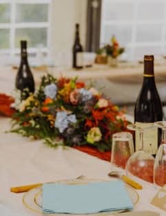 Centre de table floral coloré sur table de mariage avec bouteilles de vin et serviette bleu ciel.