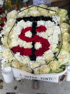 Gerbe de fleurs avec signe dollar rouge et noir et ruban À NOTRE TONTON pour un hommage de deuil.