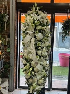 Gerbe funéraire verticale de fleurs blanches avec lys et roses, ornée d'un ruban A NOTRE TANTE pour obsèques.