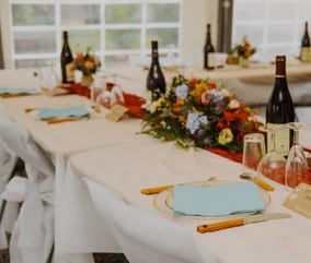 Décoration de table de mariage avec fleurs colorées, serviettes bleu ciel, bouteilles de vin et couverts élégants.